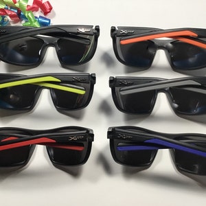 Peut inclure: Six paires de lunettes de soleil noires avec des verres fonc&eacute;s et des accents color&eacute;s sur les branches. Les branches pr&eacute;sentent des couleurs orange, jaune, grise, rouge et bleue. Les lunettes sont dispos&eacute;es en deux rang&eacute;es de trois.