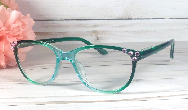 May include: Translucent teal green eyeglasses featuring a gradient frame design. The outer corners of the frames are embellished with small, round, light purple rhinestones. The inner temple arm includes the printed text UV Protection.