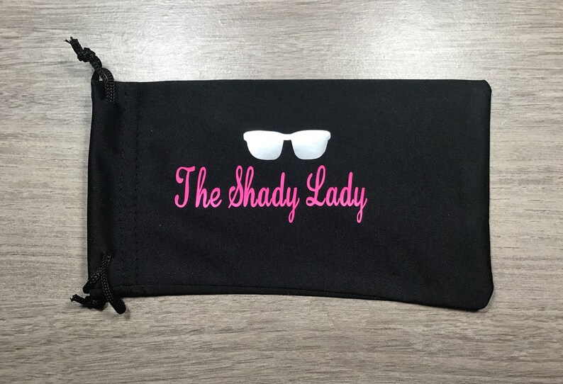 May include: Black drawstring bag with a white pair of sunglasses and the text "The Shady Lady" in pink.