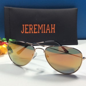 May include: Gold aviator sunglasses with orange mirrored lenses. The sunglasses are in a black case with the word "JEREMIAH" printed in orange.