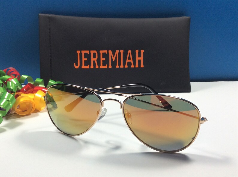 May include: Gold aviator sunglasses with orange mirrored lenses. The sunglasses are in a black case with the word "JEREMIAH" printed in orange.