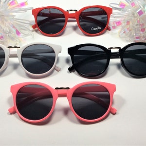 May include: Four pairs of round sunglasses with black lenses. The sunglasses are in red, white, black, and pink frames.