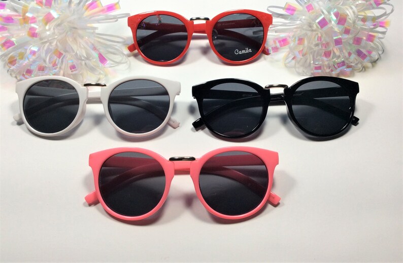 May include: Four pairs of round sunglasses with black lenses. The sunglasses are in red, white, black, and pink frames.