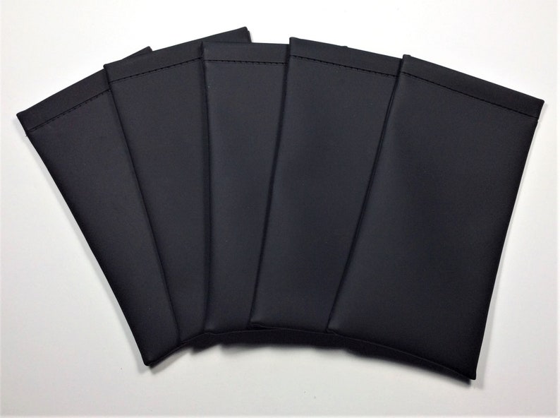 May include: Six black rectangular pouches, possibly for glasses or small electronics, are fanned out against a white background. Each pouch is made of a smooth, dark material with a stitched top edge.