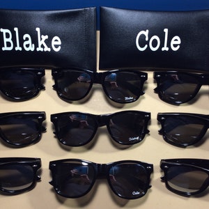 May include: Eight pairs of black sunglasses with the names "Blake" and "Cole" printed on the lenses. The sunglasses are displayed in rows of two, with each row alternating between the two names.