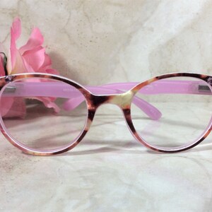 May include: A pair of eyeglasses with a pink frame and a tortoiseshell pattern on the rims. The temples are also pink. The corners of the frames are embellished with small, sparkling rhinestones. The lenses are clear.