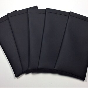 May include: A collection of six black, rectangular pouches, possibly for glasses or small electronics, are arranged in a fan shape. Each pouch is made of a smooth, dark material with a stitched top edge, suggesting a protective design.