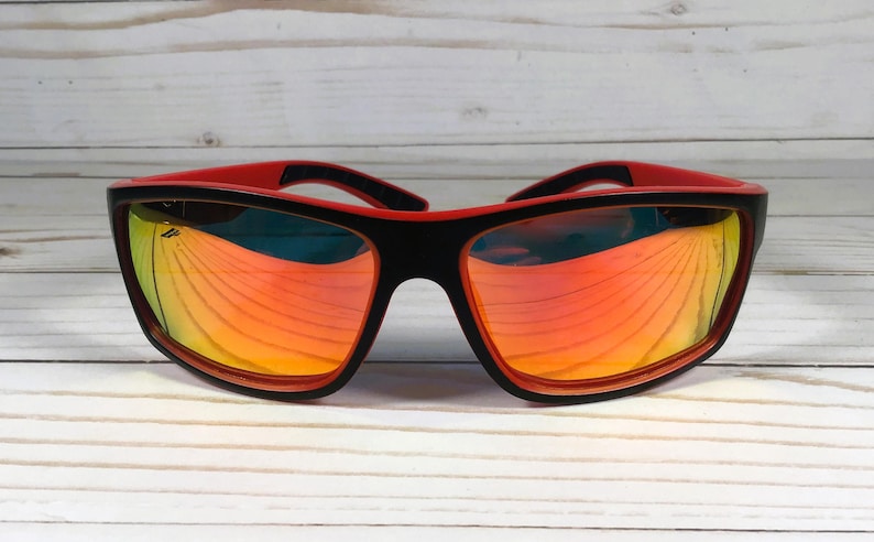 K&ouml;nnte beinhalten: Schwarze und rote Sonnenbrille mit reflektierendem orangefarbenem Glas. Die Sonnenbrille hat ein sportliches Design.