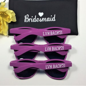 May include: Three pairs of purple sunglasses with black lenses. Each pair has the text "LVH BACH'21" printed on the arms in white.
