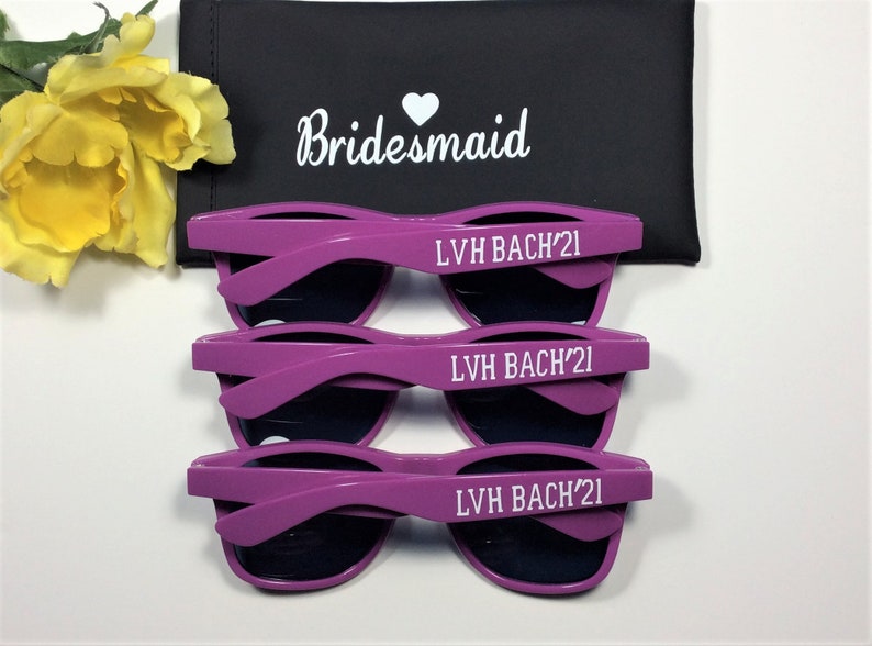May include: Three pairs of purple sunglasses with black lenses. Each pair has the text "LVH BACH'21" printed on the arms in white.