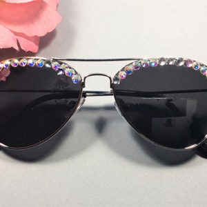 Pu&ograve; includere: Occhiali da sole aviator argentati con lenti nere e una fila di strass iridescenti attorno alla parte superiore delle montature. Gli occhiali da sole hanno un'etichetta "Made in China" sull'asta destra.