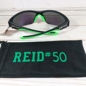 May include: Black sunglasses with green accents and mirrored lenses. The sunglasses are paired with a black drawstring bag with the text "REID#50" in green. The sunglasses have the word "FORCE" on the side.