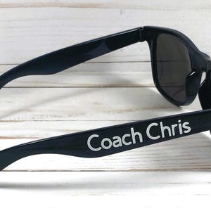 May include: Black sunglasses with the text "Coach Chris" printed on the side.