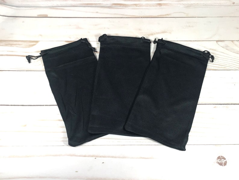 May include: Three black drawstring pouches made of soft fabric. The pouches are lying flat on a white wooden surface.