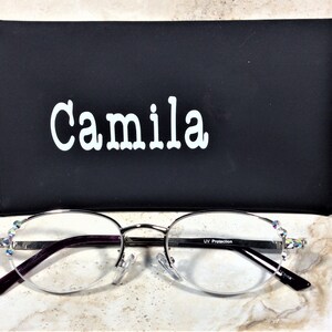 May include: Silver-framed spectacles with a black case. The spectacles have a half-rim design with clear lenses and purple arms. The case is black with the name "Camila" in white lettering. The spectacles have decorative rhinestones.