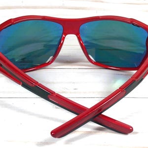 May include: Red sunglasses with blue mirrored lenses. The sunglasses have a black stripe on the arms.