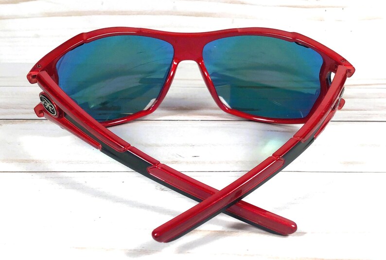May include: Red sunglasses with blue mirrored lenses. The sunglasses have a black stripe on the arms.