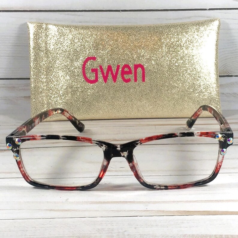 Pu&ograve; includere: Occhiali rettangolari con montatura fantasia rossa, nera e bianca e lenti trasparenti. La montatura ha strass decorativi. Dietro gli occhiali c'&egrave; un astuccio dorato con il nome "Gwen" in lettere rosa.