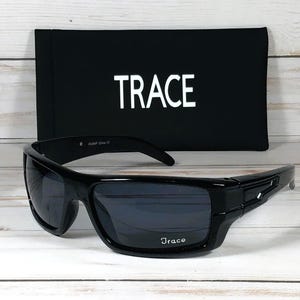 May include: Black sunglasses with dark lenses and a matching black case. The sunglasses have a rectangular frame with the brand name "Trace" printed on the lens and case. The case is black with the word "TRACE" in white.