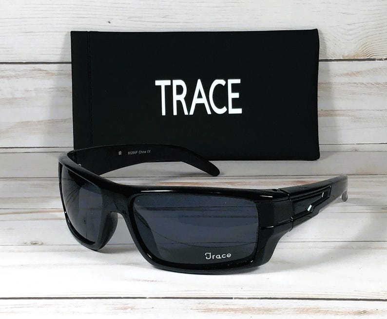 May include: Black sunglasses with dark lenses and a matching black case. The sunglasses have a rectangular frame with the brand name "Trace" printed on the lens and case. The case is black with the word "TRACE" in white.