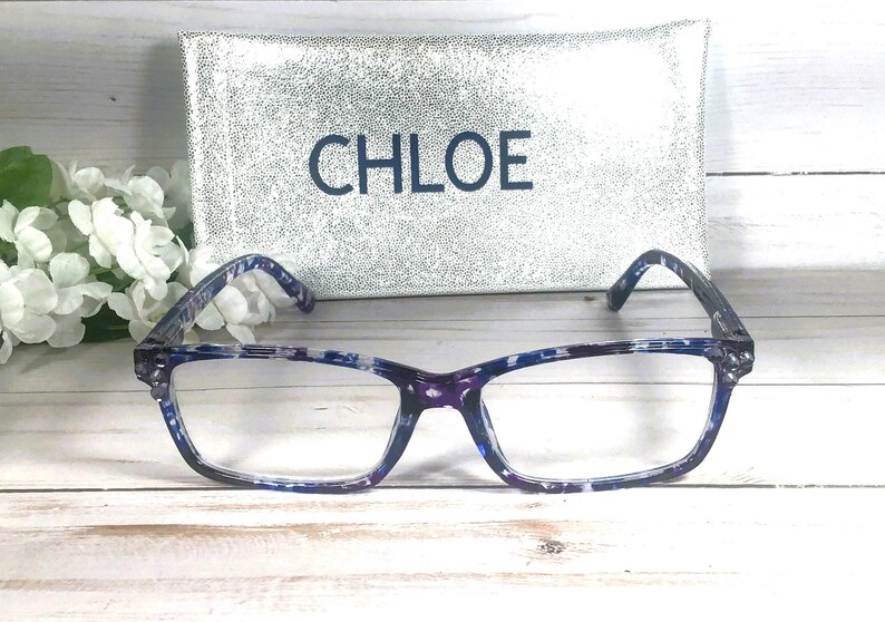Peut inclure: Lunettes rectangulaires avec une monture &agrave; motif &eacute;caille de tortue bleu et violet. Derri&egrave;re les lunettes se trouve un &eacute;tui rectangulaire argent&eacute; &agrave; paillettes avec le mot CHLOE imprim&eacute; en lettres bleu fonc&eacute; sur la face avant de l'&eacute;tui.