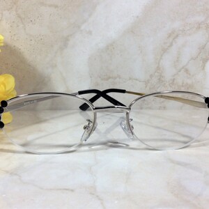 May include: Silver-rimmed eyeglasses with a half-frame design. The frames feature black embellishments on the outer corners. The lenses are clear, and the bridge and temples are a silver and black color. The text "2319 +1.50" is printed on the frame.