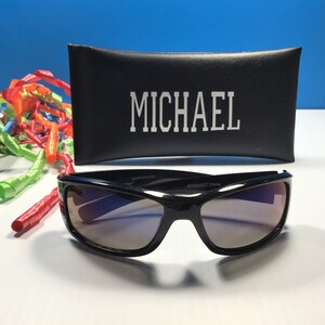 May include: Black sunglasses with a dark tinted lens and a black case with the name "MICHAEL" printed on it.