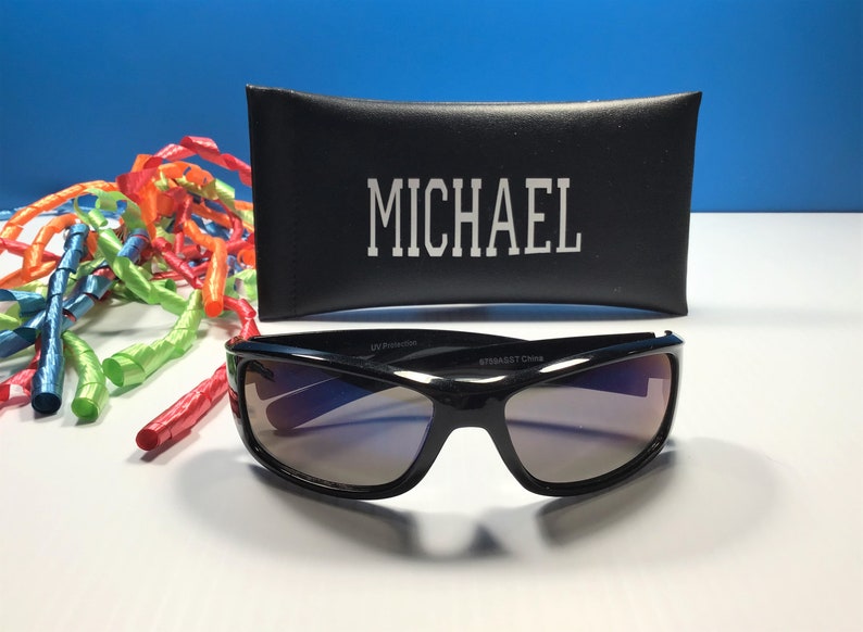 May include: Black sunglasses with a dark tinted lens and a black case with the name "MICHAEL" printed on it.