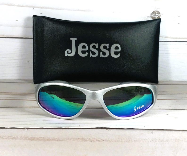 Op de afbeelding: Zilverkleurige zonnebril met iriserende, meerkleurig reflecterende glazen met de naam Jesse op het rechterglas gedrukt. De zonnebril wordt geleverd met een zwart rechthoekig beschermend etui met de naam Jesse in zilverkleurige letters.