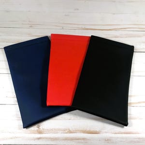 Puede incluir: Tres estuches para gafas en azul marino, rojo y negro. Los estuches son rectangulares y parecen estar hechos de un material suave y liso. Est&aacute;n colocados sobre una superficie de madera blanca.