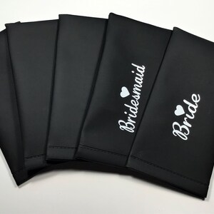 May include: Six black fabric pouches with white text and a small heart. The pouches are labeled "Bride" and "Bridesmaid".