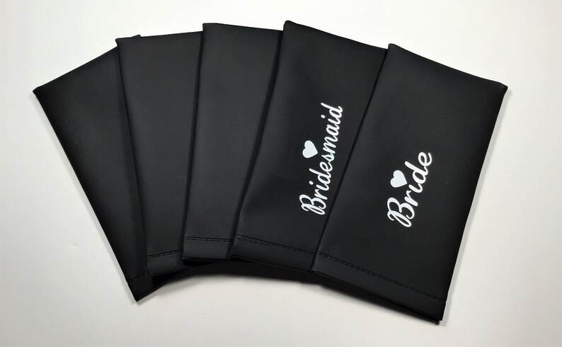 May include: Six black fabric pouches with white text and a small heart. The pouches are labeled "Bride" and "Bridesmaid".