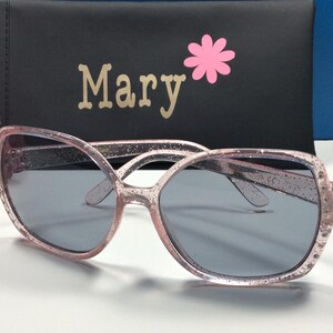 May include: Pink glitter sunglasses with a black case that says "Mary" on it with a pink flower.