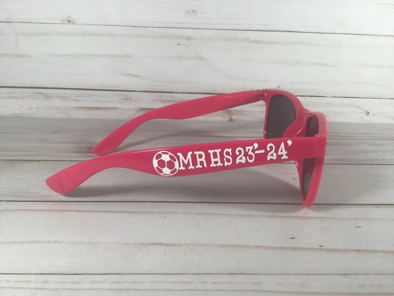 May include: Pink sunglasses with a white soccer ball and the text "MRHS 23-24" on the side.