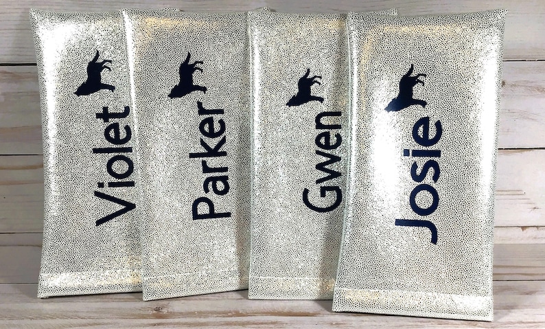 Pu&ograve; includere: Quattro sacchetti color argento con un motivo strutturato e puntinato. Ogni sacchetto presenta una silhouette blu scuro e un nome stampato in blu scuro: Violet, Parker, Gwen e Josie. I sacchetti sono in piedi.
