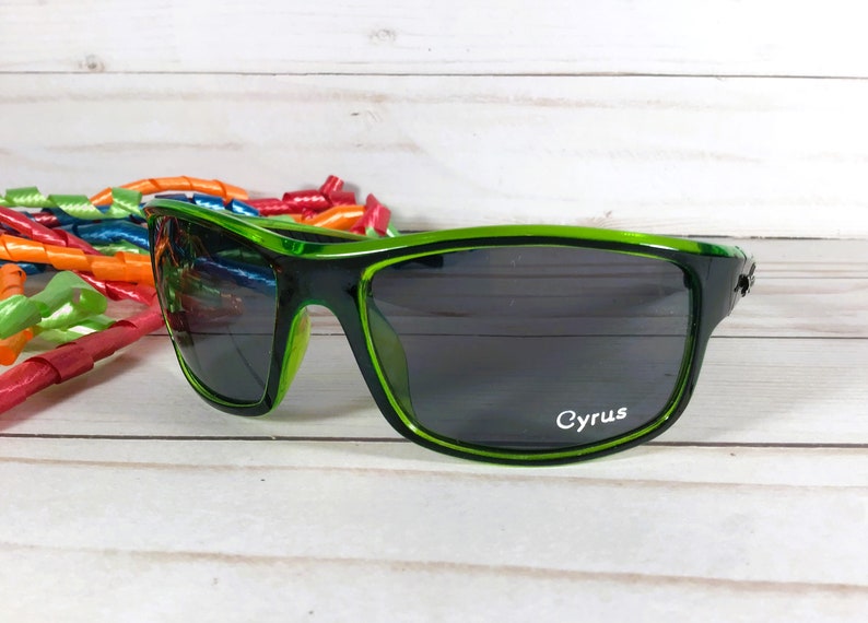 K&ouml;nnte beinhalten: Gr&uuml;ne Sonnenbrille mit dunklen Gl&auml;sern und dem Wort "Cyrus" auf dem rechten Glas.