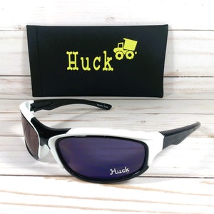 Peut inclure: Lunettes de soleil blanches et noires avec des verres violets. Les lunettes de soleil ont le mot "Huck" imprim&eacute; sur les verres. Les lunettes de soleil sont livr&eacute;es avec un &eacute;tui noir sur lequel est imprim&eacute; le mot "Huck" et un camion &agrave; benne basculante jaune.