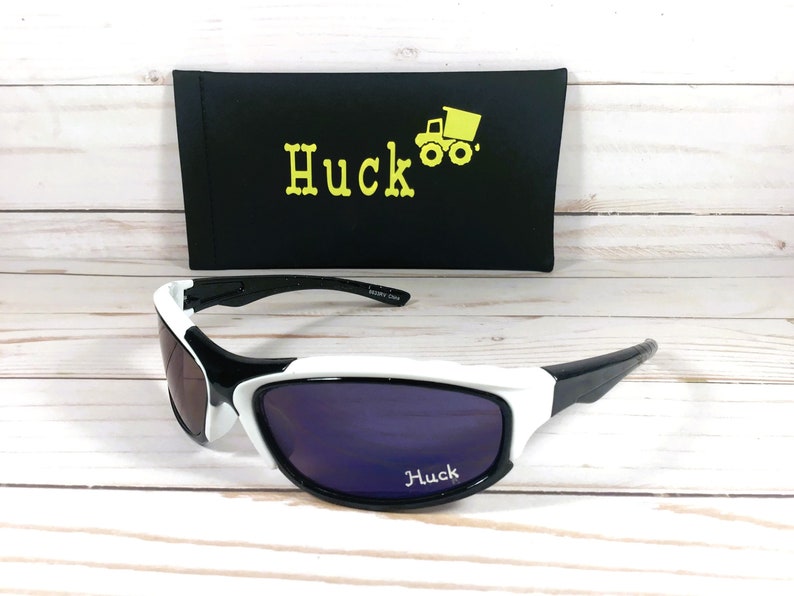 Peut inclure: Lunettes de soleil blanches et noires avec des verres violets. Les lunettes de soleil ont le mot "Huck" imprim&eacute; sur les verres. Les lunettes de soleil sont livr&eacute;es avec un &eacute;tui noir sur lequel est imprim&eacute; le mot "Huck" et un camion &agrave; benne basculante jaune.
