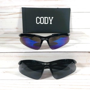 May include: Black sunglasses with a blue mirrored lens and a black case with the name "CODY" printed on it.