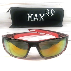 May include: Black and red sunglasses with mirrored lenses. The sunglasses are paired with a black carrying case with the word "MAX" in white and a baseball graphic. The sunglasses have a sporty design.