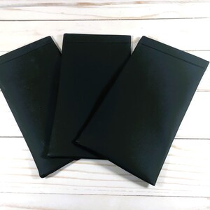 May include: Three black fabric pouches, possibly for glasses or other small items, are stacked on a white wooden surface.
