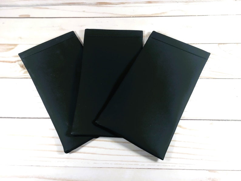 May include: Three black fabric pouches, possibly for glasses or other small items, are stacked on a white wooden surface.