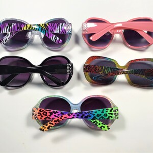 May include: Four pairs of sunglasses with different animal print designs. The sunglasses have a rounded shape and are decorated with rhinestones. The frames are in various colors, including pink, black, and clear.