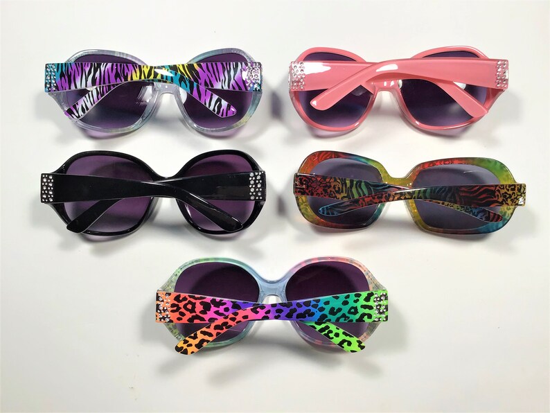 May include: Four pairs of sunglasses with different animal print designs. The sunglasses have a rounded shape and are decorated with rhinestones. The frames are in various colors, including pink, black, and clear.