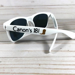 May include: White sunglasses with black lenses and the text "Canon's 18!" printed on the side. A brown boot icon is next to the text.