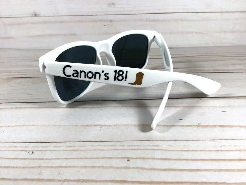 May include: White sunglasses with black lenses and the text "Canon's 18!" printed on the side. A brown boot icon is next to the text.