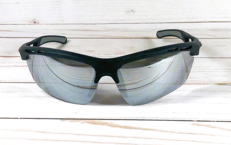 May include: Sport sunglasses featuring a matte black frame and reflective silver mirrored lenses. The design includes a wrap-around style with ventilated side temples and a contoured bridge, providing a wide field of vision for outdoor activities.
