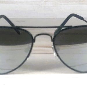 May include: Aviator sunglasses featuring a thin matte black metal frame with a double bridge design. The lenses are highly reflective and silver in color, providing a mirror-like finish. The temples are thin and black with curved ear pieces.