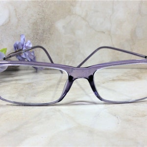 May include: Rectangular eyeglasses with a translucent purple frame. The outer corners of the frame are embellished with small, sparkling pink and clear rhinestones. The temples are thin and match the purple color of the front frame.
