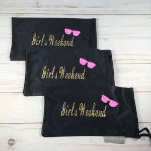 May include: Three black eyeglass cases with a gold glitter inscription that reads "Girls Weekend" and a pink glitter image of sunglasses. The bottom case has a small white tag that reads "FASHION COLLECTION".